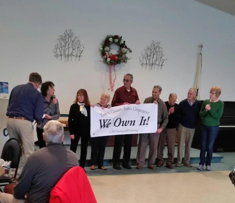 Photo showing community leaders holding We Own It! Banner during community celebration.