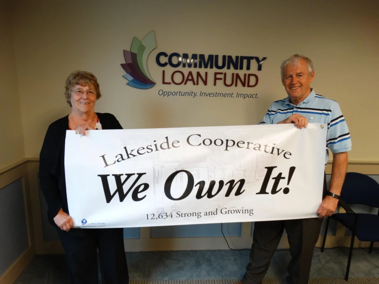 Photo of Pauline Gordon, Lakeside Treasurer; and Roland Shattuck, Lakeside President, holding a We Own It! banner at the Community Loan Fund in Concord.